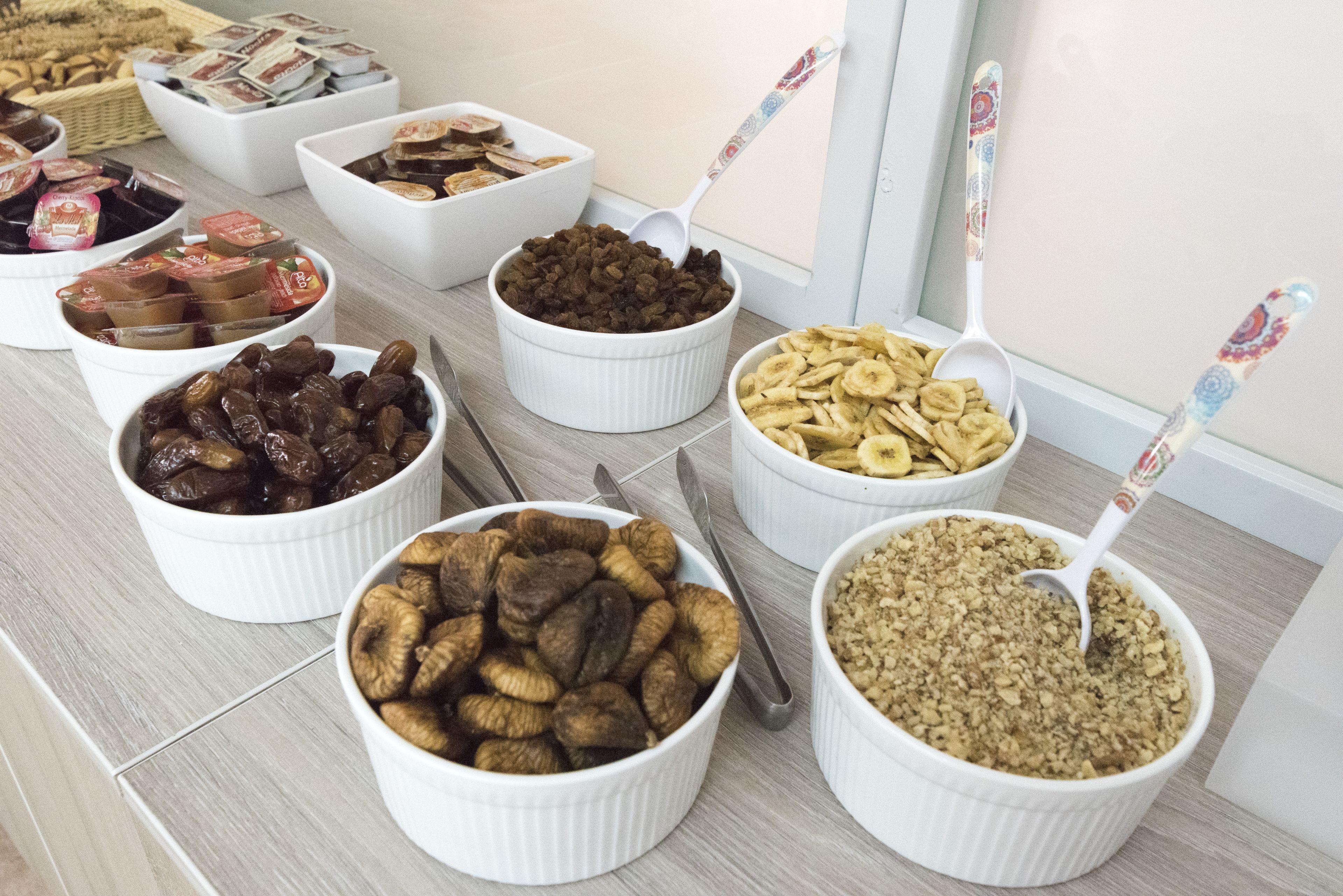 Diversos alimentos en recipientes blancos con cucharas, sobre una mesa.