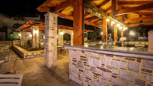 Un área de bar al aire libre con pilares de piedra, vigas de madera y chimenea de piedra.