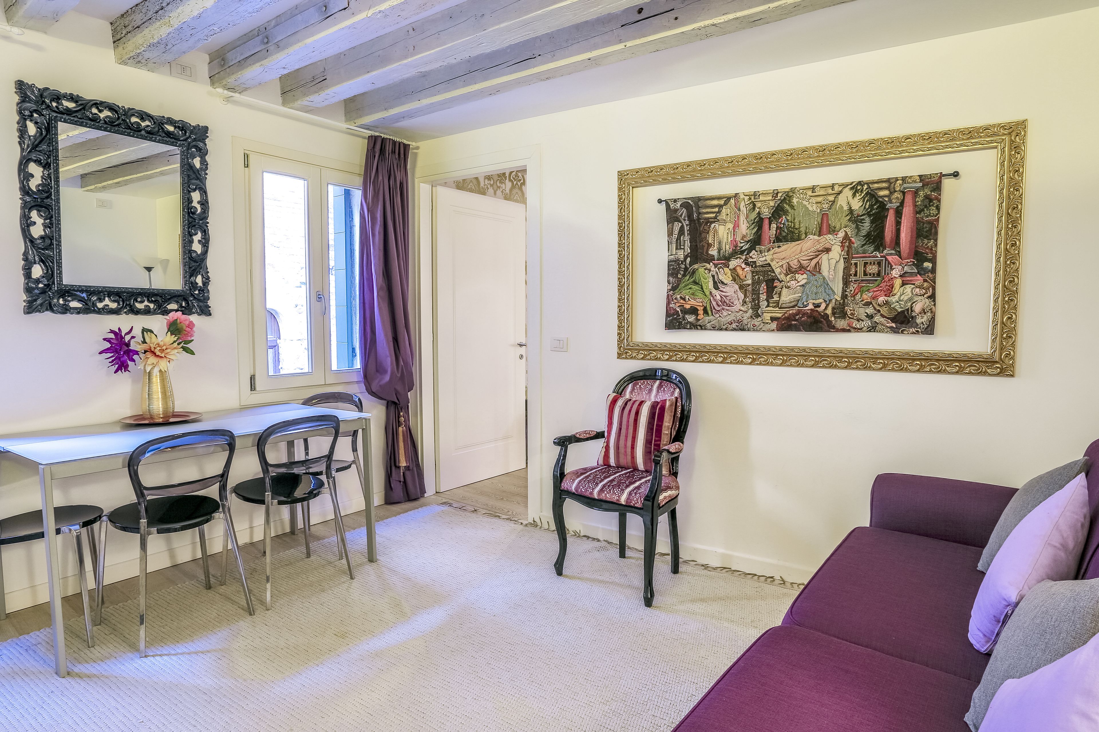 A room with a dining area, a sofa, and a framed painting.