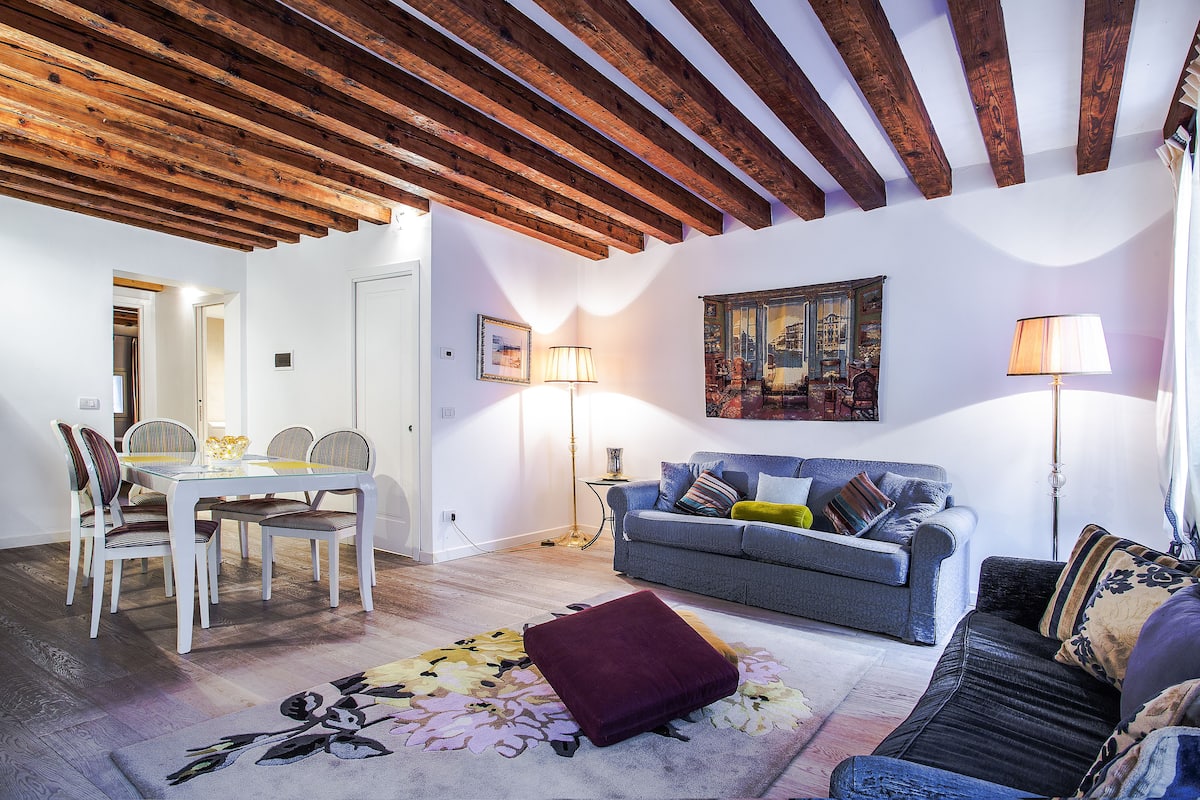 Uma sala de estar com mesa de jantar, sofá e uma pintura grande na parede.