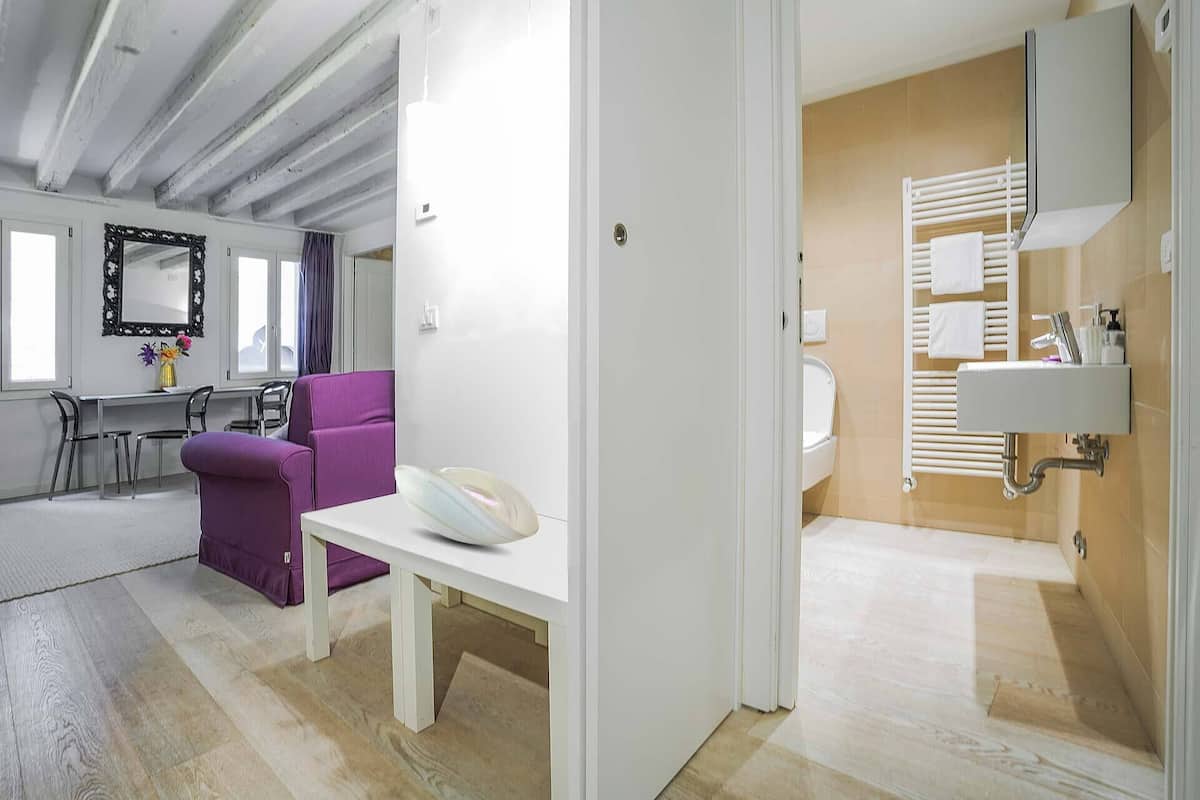 Quarto de hotel moderno com área de refeições, banheiro com porta-toalhas e um espelho grande.