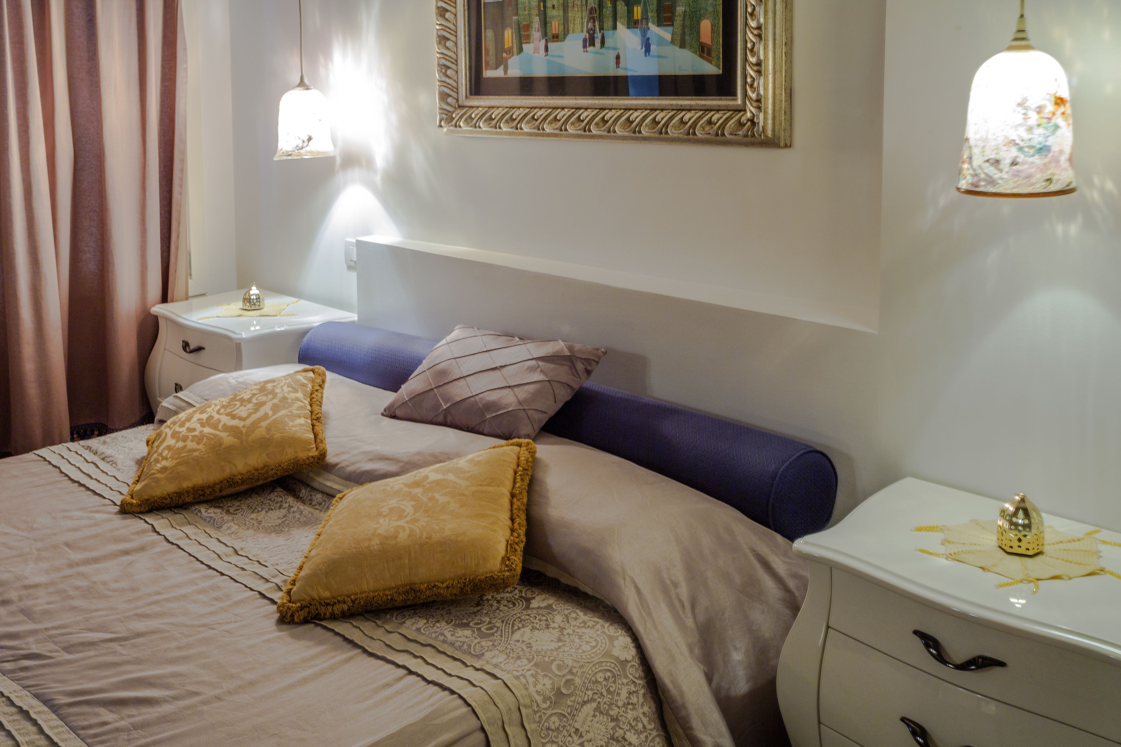 A neatly arranged bedroom with a large bed, two bedside tables, a nightstand, and a wall-mounted picture.