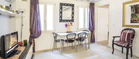 Une pièce avec un téléviseur, une table avec des chaises, un miroir et un tableau encadré au mur.