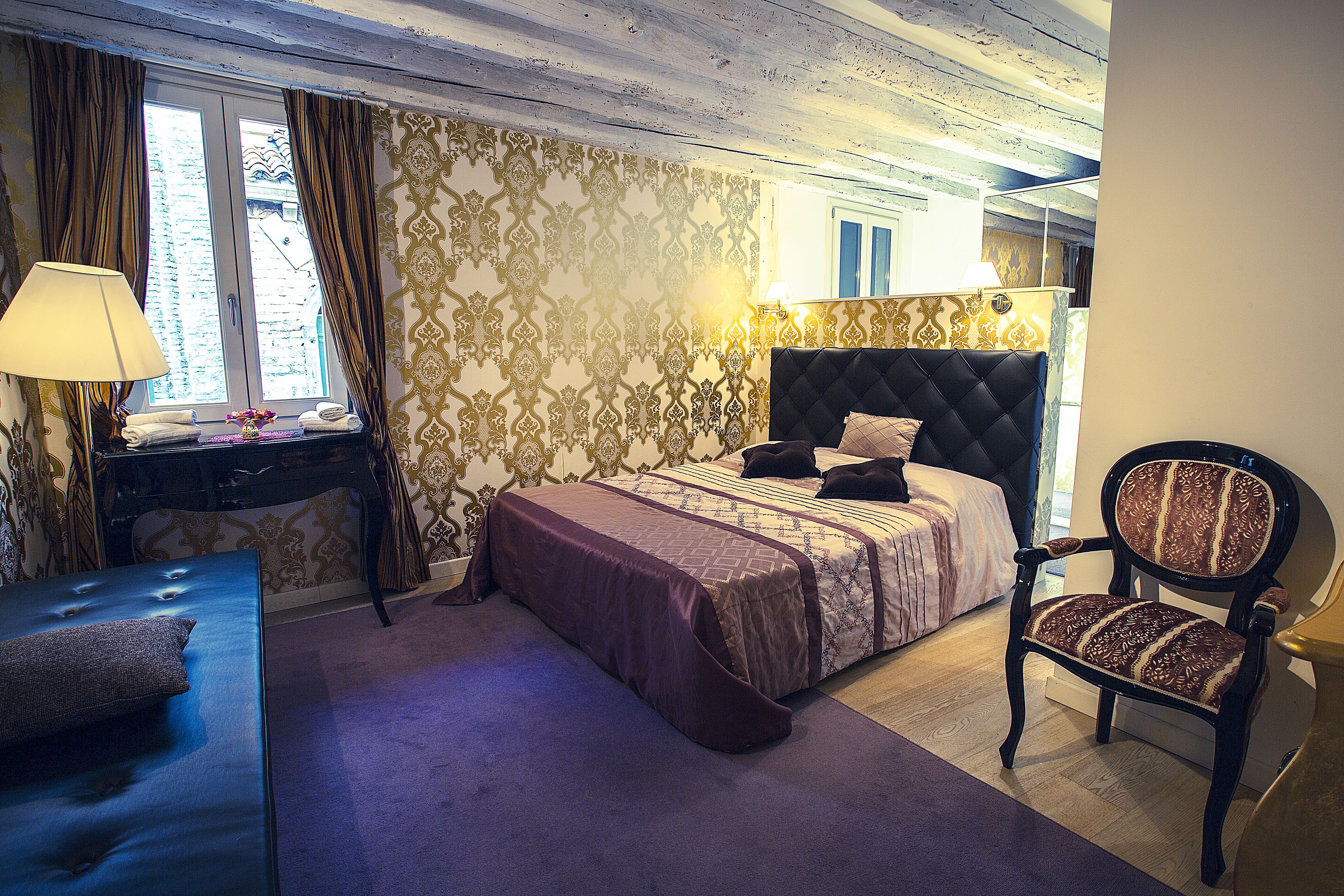 A bedroom with a bed, a chair, a desk, and a window with curtains.