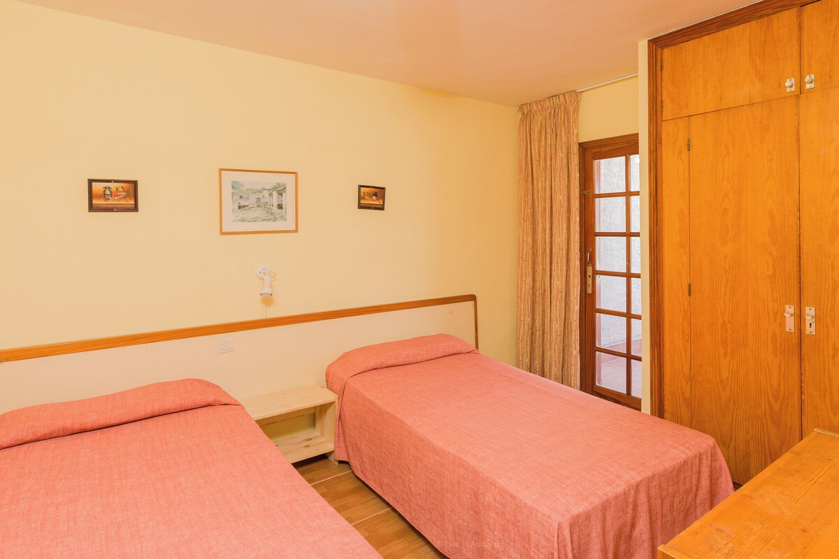 A room with two single beds, wooden wardrobe, and a window with curtains.