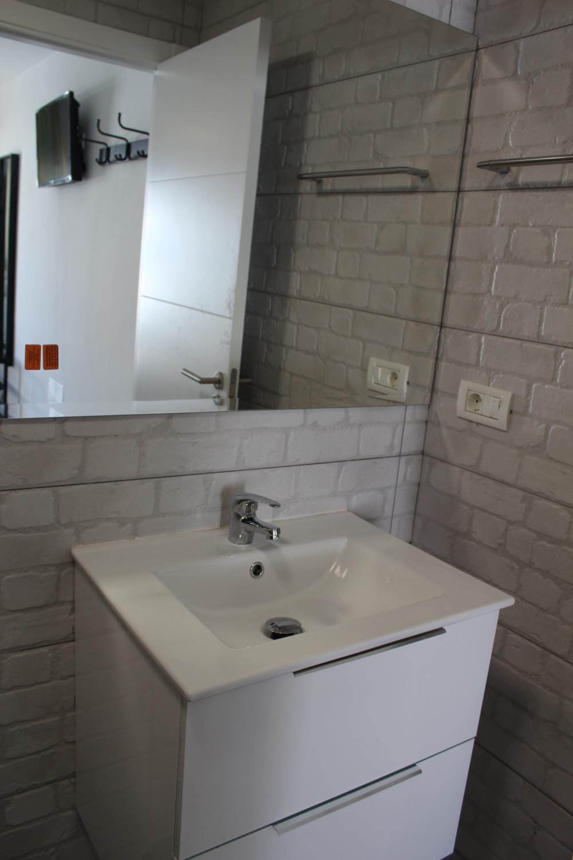 Un bagno con lavandino bianco, uno specchio e zona doccia.