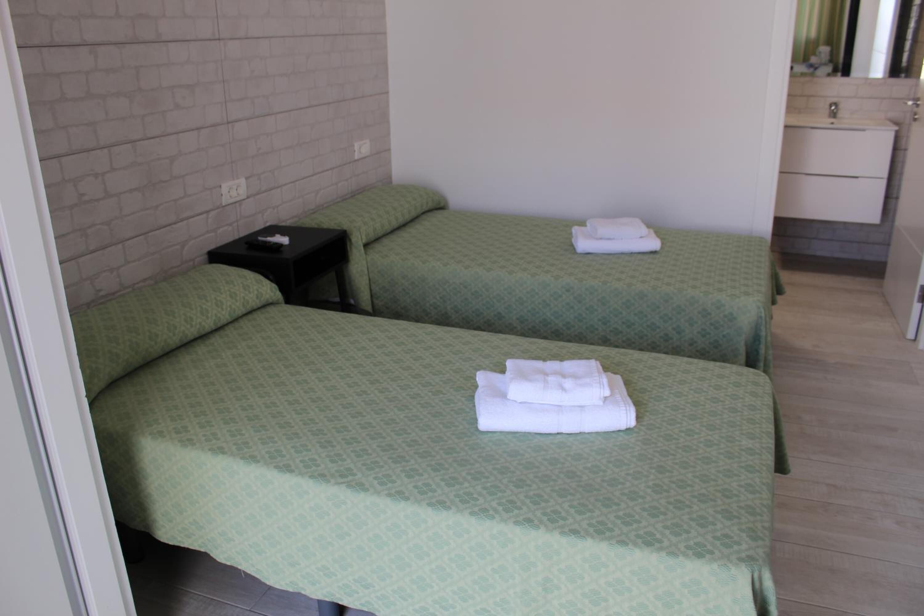 A hotel room with two single beds, a small bedside table, a nightstand, and a bathroom with a sink and mirror.