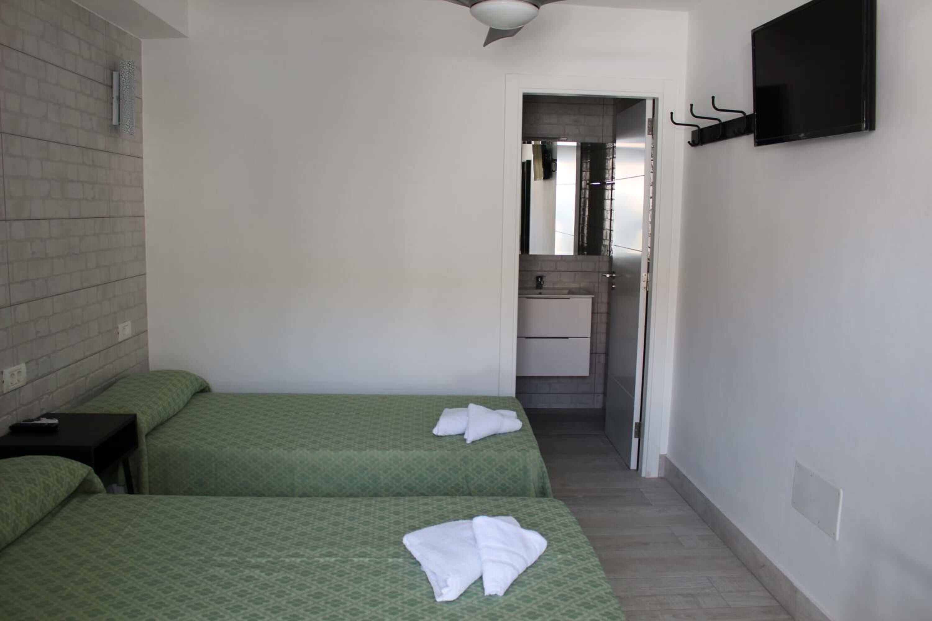 Ett hotellrum med två sängar, en tv som hänger på väggen, ett badrum som syns genom en öppen dörr och en handduk på varje säng.