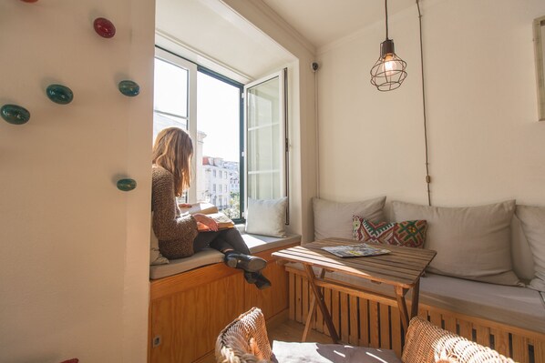 Een gezellige kamer met een houten tafel, een bank en een raam met uitzicht op een stadsgezicht.