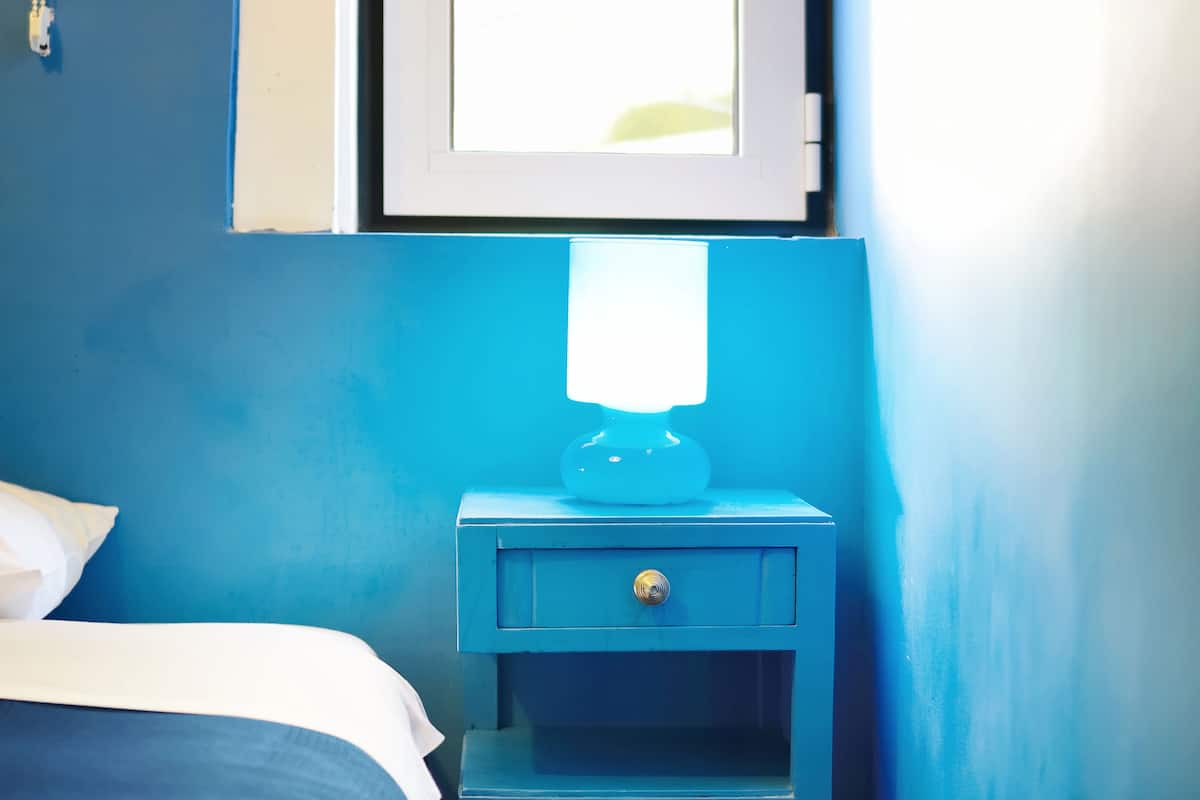 Een slaapkamer met een bed, een nachtkastje met een lamp en een raam.