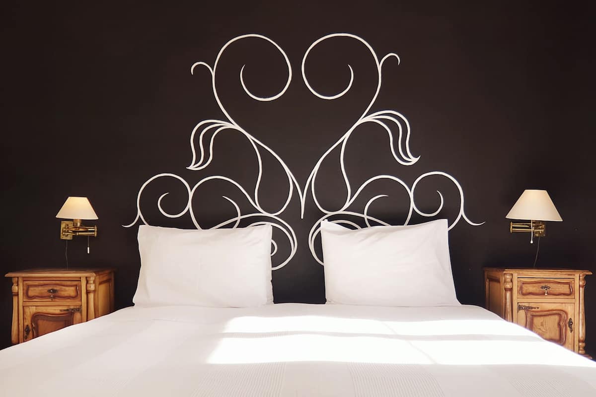 Een bed met een wit hoofdeinde en twee nachtkastjes met lampen.