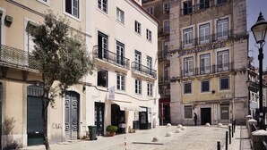 Une rue pavée bordée de bâtiments historiques, avec un arbre et un ciel dégagé.