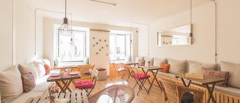 Un salón luminoso con muebles de mimbre, una mesa de centro de madera y un sofá. Varias ventanas dejan entrar luz natural, y hay un espejo en la pared.