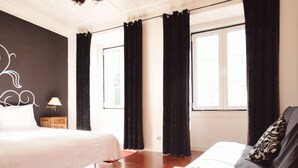 Une chambre à coucher avec un lit, une chaise, une table de chevet, une lampe et une fenêtre avec des rideaux.
