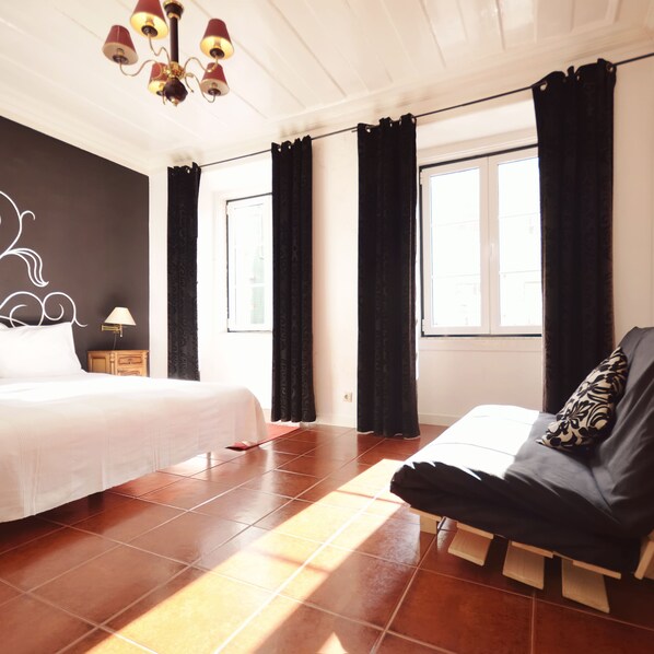 A bedroom with a bed, a chair, a nightstand, a lamp, and a window with curtains. - Lisbon Story Guesthouse (Lisbon)