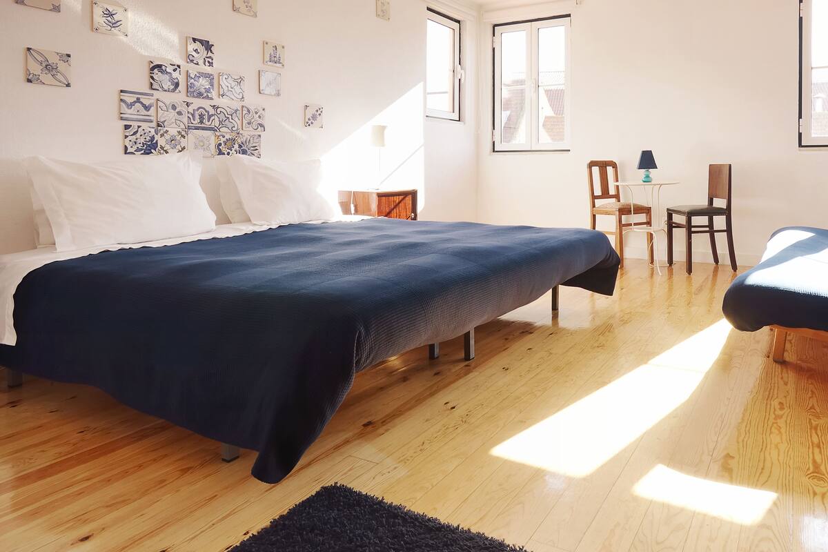 Een slaapkamer met een bed, een bureau en stoelen, houten vloeren en een raam.