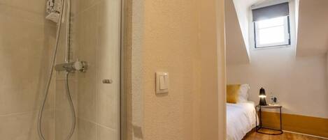 Ein Hotelzimmer mit Dusche, einem Bett, einem Nachttisch mit Lampe und einem Fenster.