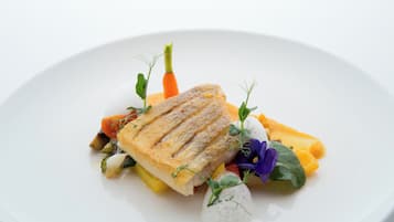 Un plato blanco con pescado a la parrilla, verduras y una flor decorativa.