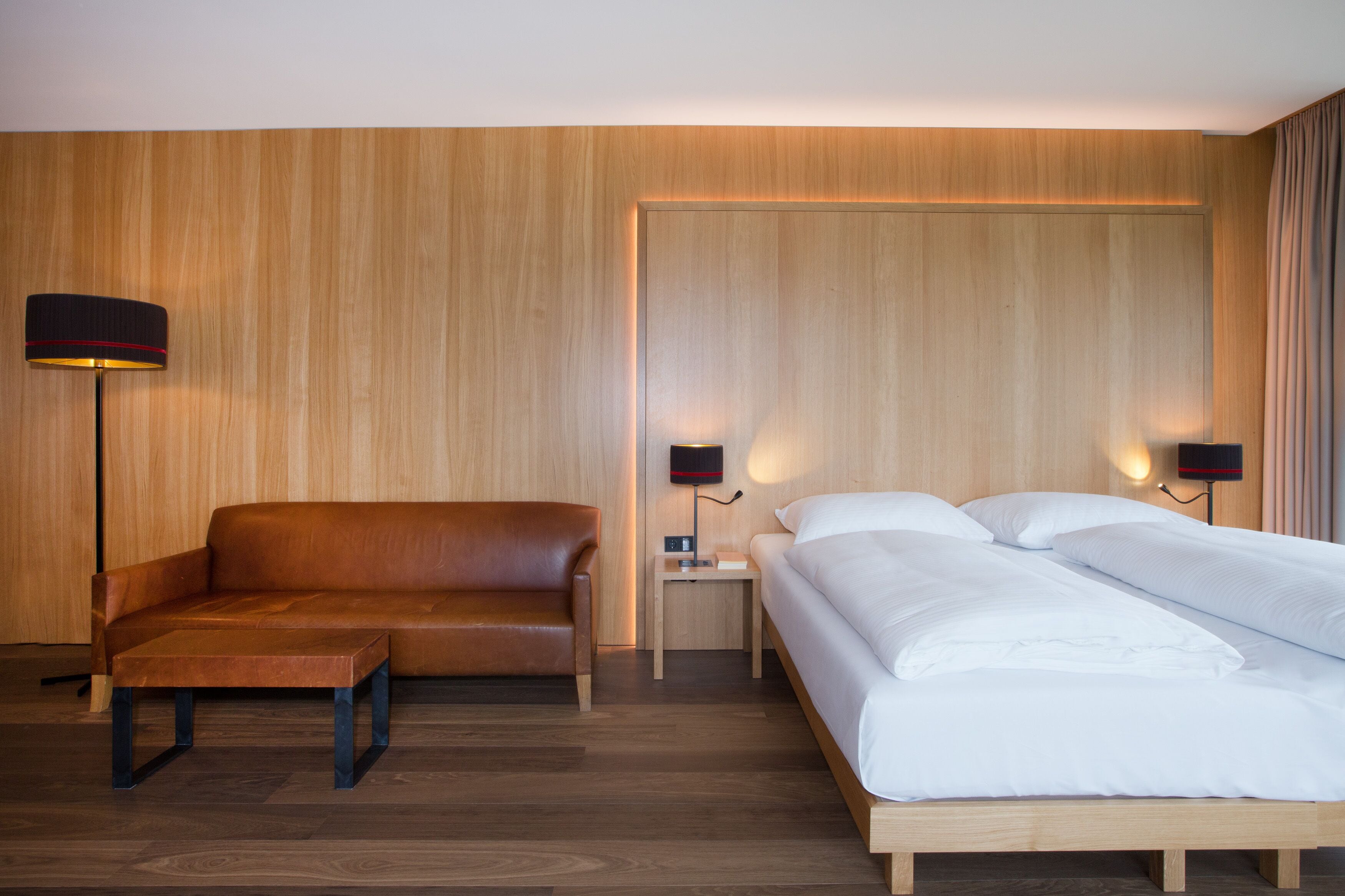 Een hotelkamer met een houten wand, een bruine leren bank, een houten bed en twee bedlampjes.