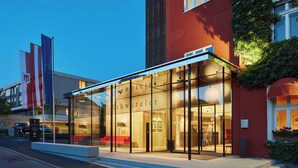 Un hotel modern amb façana de vidre, exterior vermell i un rètol que indica que és restaurant i zona d'aparcament.