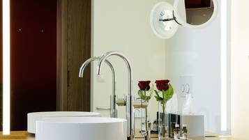 Une salle de bain moderne avec un lavabo rond, deux robinets, un miroir et deux vases de roses.