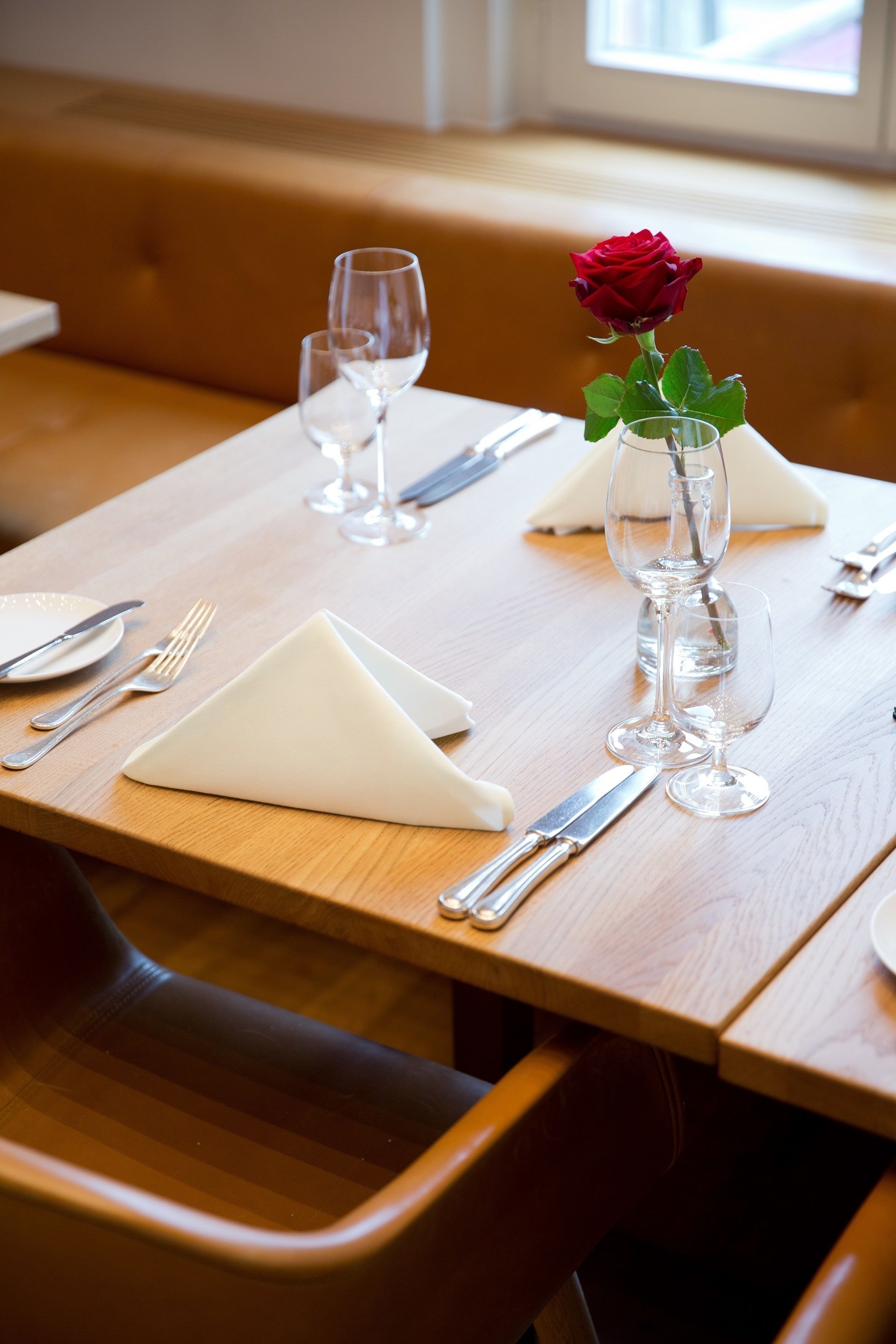 A dining table with a rose in a glass vase, set with cutlery and a napkin.