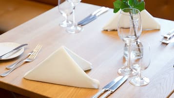 A dining table with a rose in a glass vase, set with cutlery and a napkin.