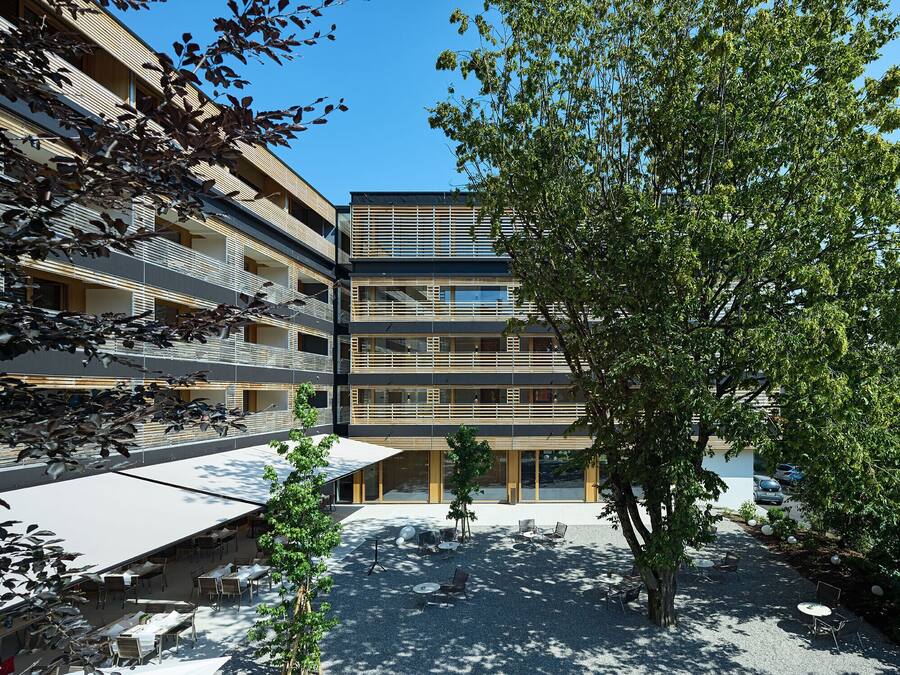 Un edificio moderno con varios pisos, zonas de estar al aire libre y un árbol en el patio.