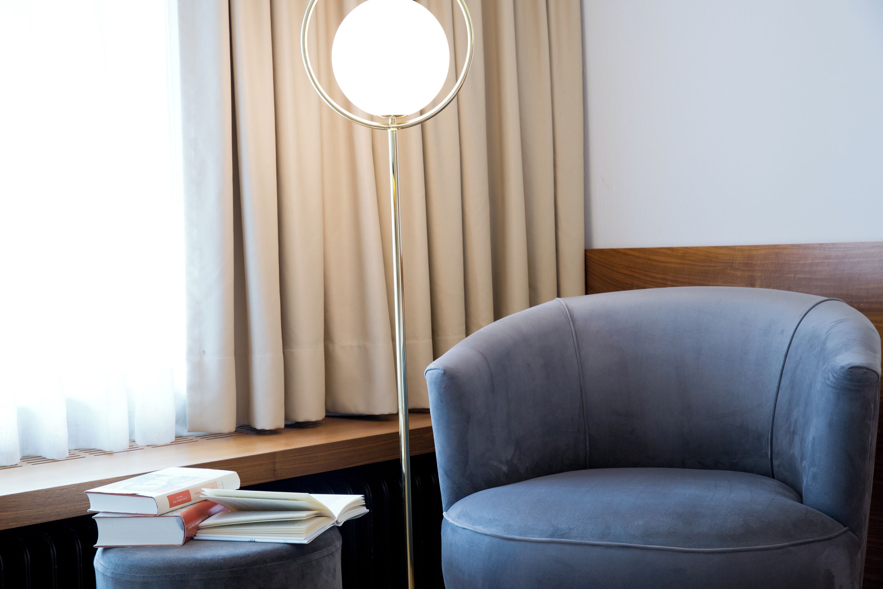 Una habitación con un sillón gris, una lámpara de pie y una ventana con cortinas.