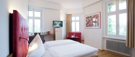 Una habitación de hotel con cama, televisión, escritorio y silla, y ventana con cortinas.