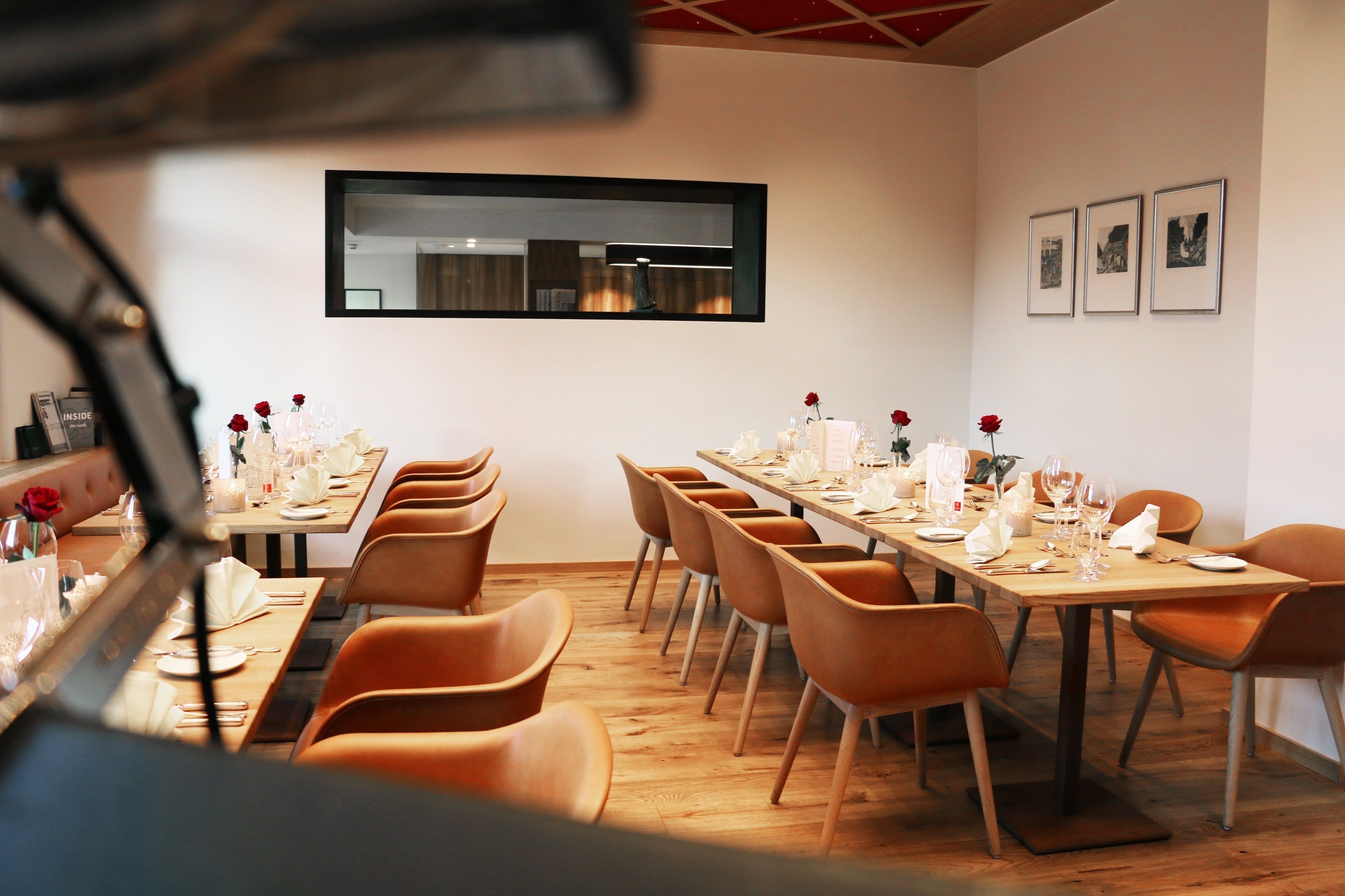 A dining area with wooden tables and orange chairs, a large mirror on the wall, and framed pictures above the tables.