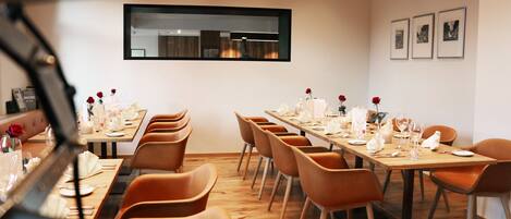 A dining area with wooden tables and orange chairs, a large mirror on the wall, and framed pictures above the tables.