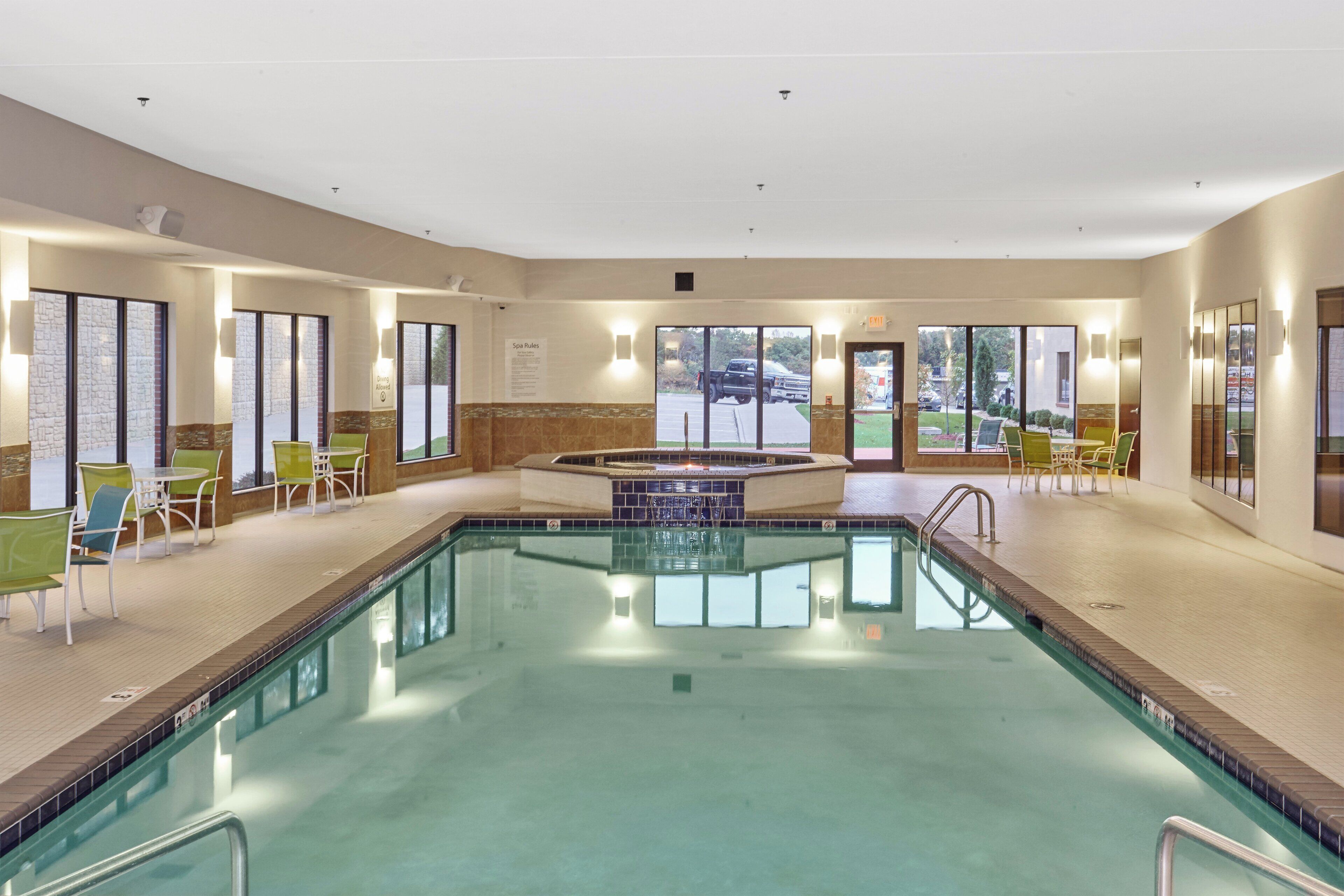 Una piscina con hidromasaje, rodeada de sillas y mesas, y grandes ventanales que ofrecen vistas al exterior.