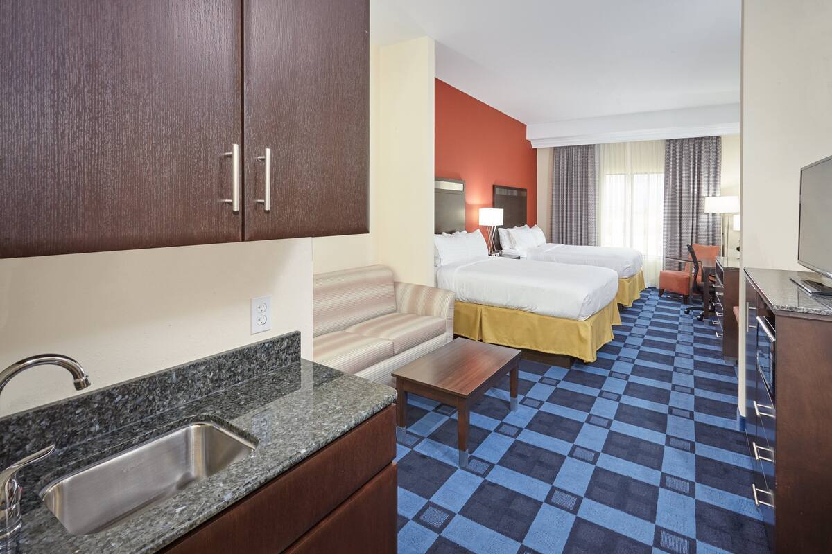 Une chambre d’hôtel avec un lit double, un canapé, une petite table, un lavabo et un téléviseur.