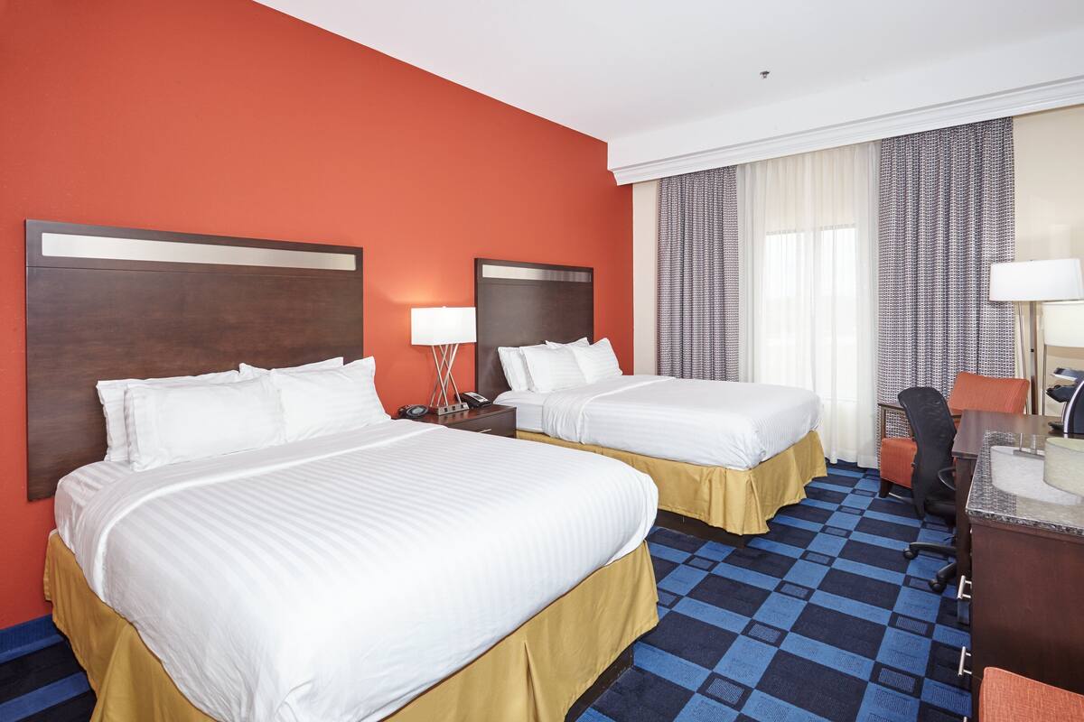 Une chambre d’hôtel avec deux lits, un bureau, une chaise et une fenêtre avec des rideaux.
