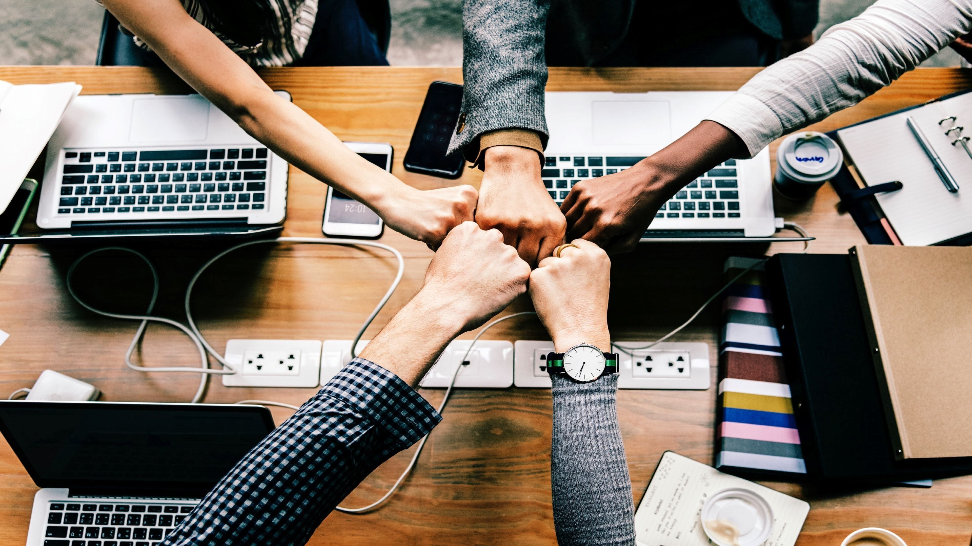 Un grupo de personas juntando las manos alrededor de una mesa con portátiles, sugiriendo un ambiente colaborativo.