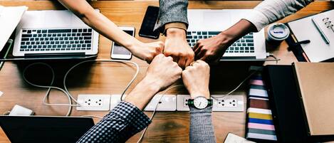 Un grupo de personas juntando las manos alrededor de una mesa con portátiles, sugiriendo un ambiente colaborativo.