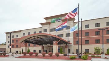 A Holiday Inn Express & Suites building with a covered entrance, multiple flags, and a landscaped area with shrubs.