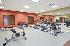 Een fitnessruimte met loopbanden, elliptische trainers en gewichten.