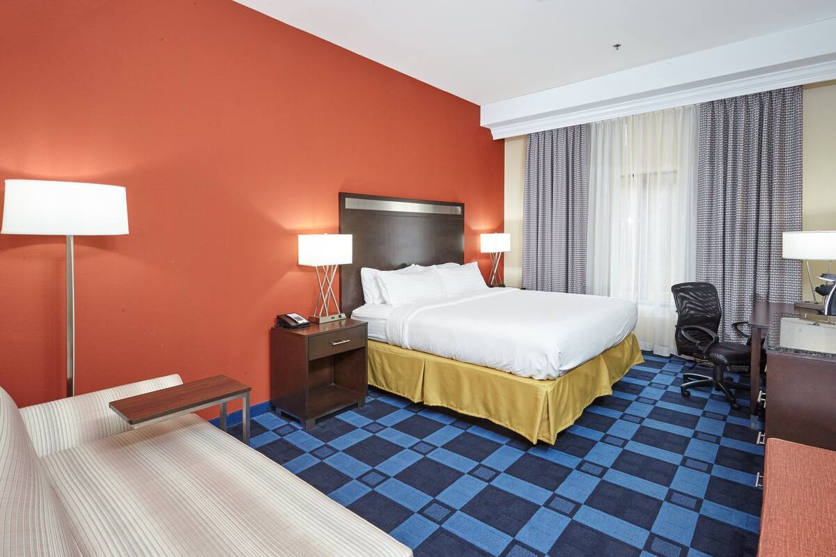 Une chambre d’hôtel avec un grand lit, deux tables de chevet avec des lampes, un bureau, une chaise et un canapé.
