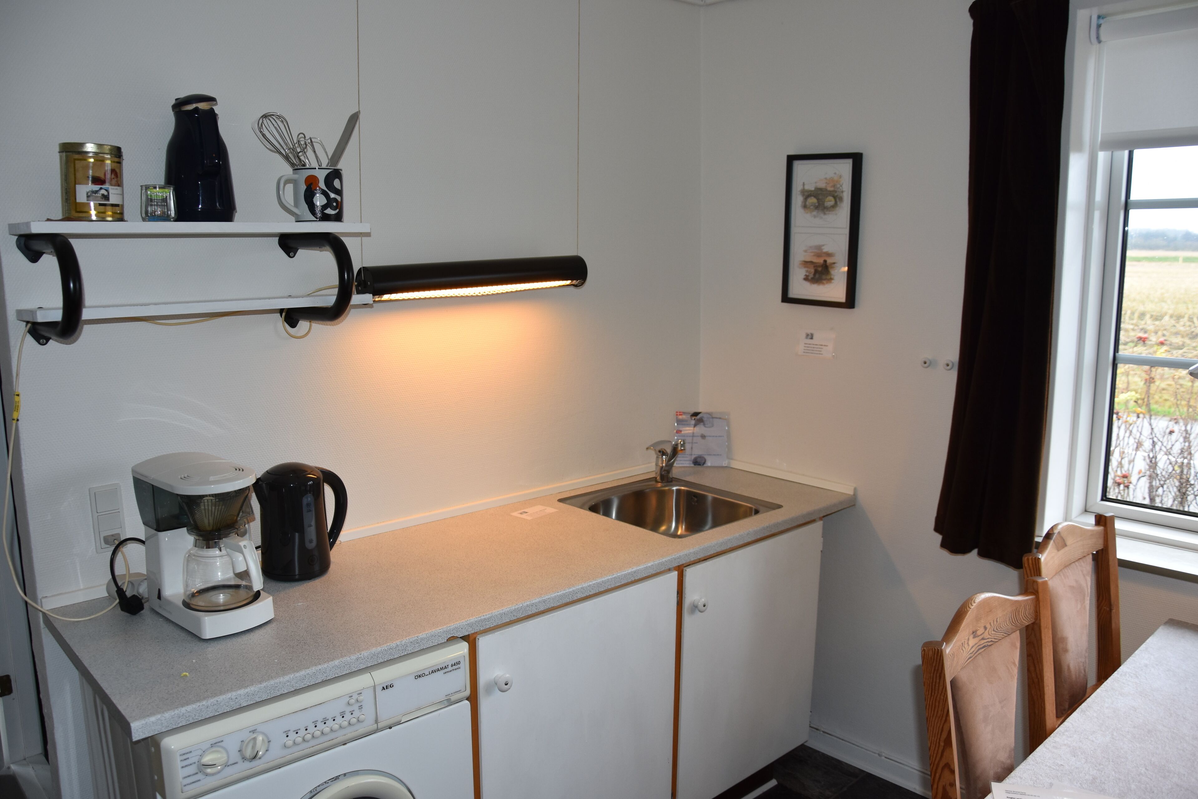 Una cocina compacta con cafetera, hervidor y un pequeño estante con utensilios de cocina.