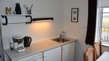 Una cocina compacta con cafetera, hervidor y un pequeño estante con utensilios de cocina.