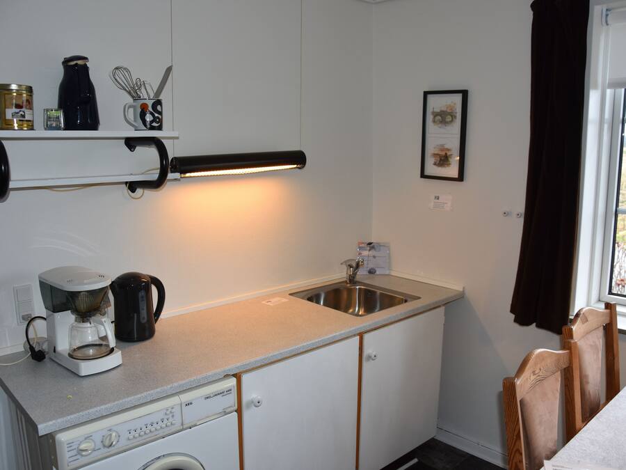 A compact kitchen with a coffee maker, kettle, and a small shelf with kitchen items.