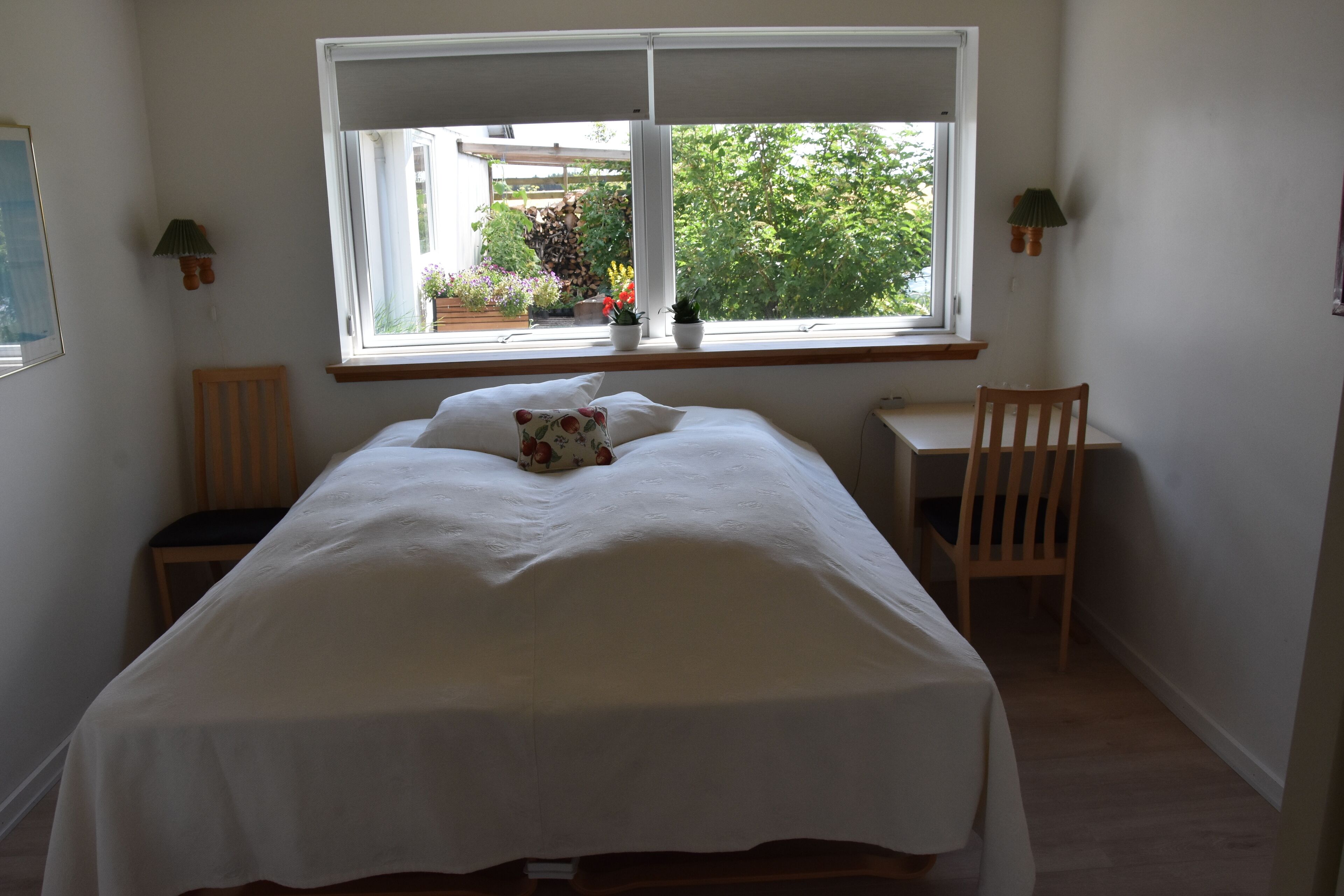 Un dormitorio con cama, escritorio y ventana con vistas a un jardín.