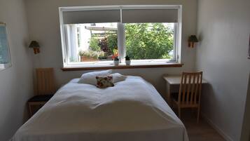 Un dormitorio con cama, escritorio y ventana con vistas a un jardín.