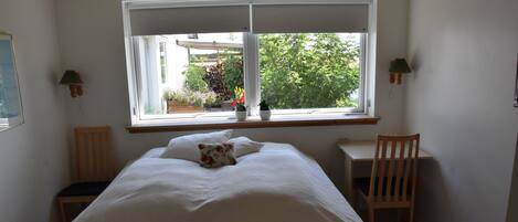 A bedroom with a bed, a desk, and a window overlooking a garden.