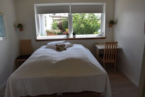 Un dormitorio con cama, escritorio y ventana con vistas a un jardín.