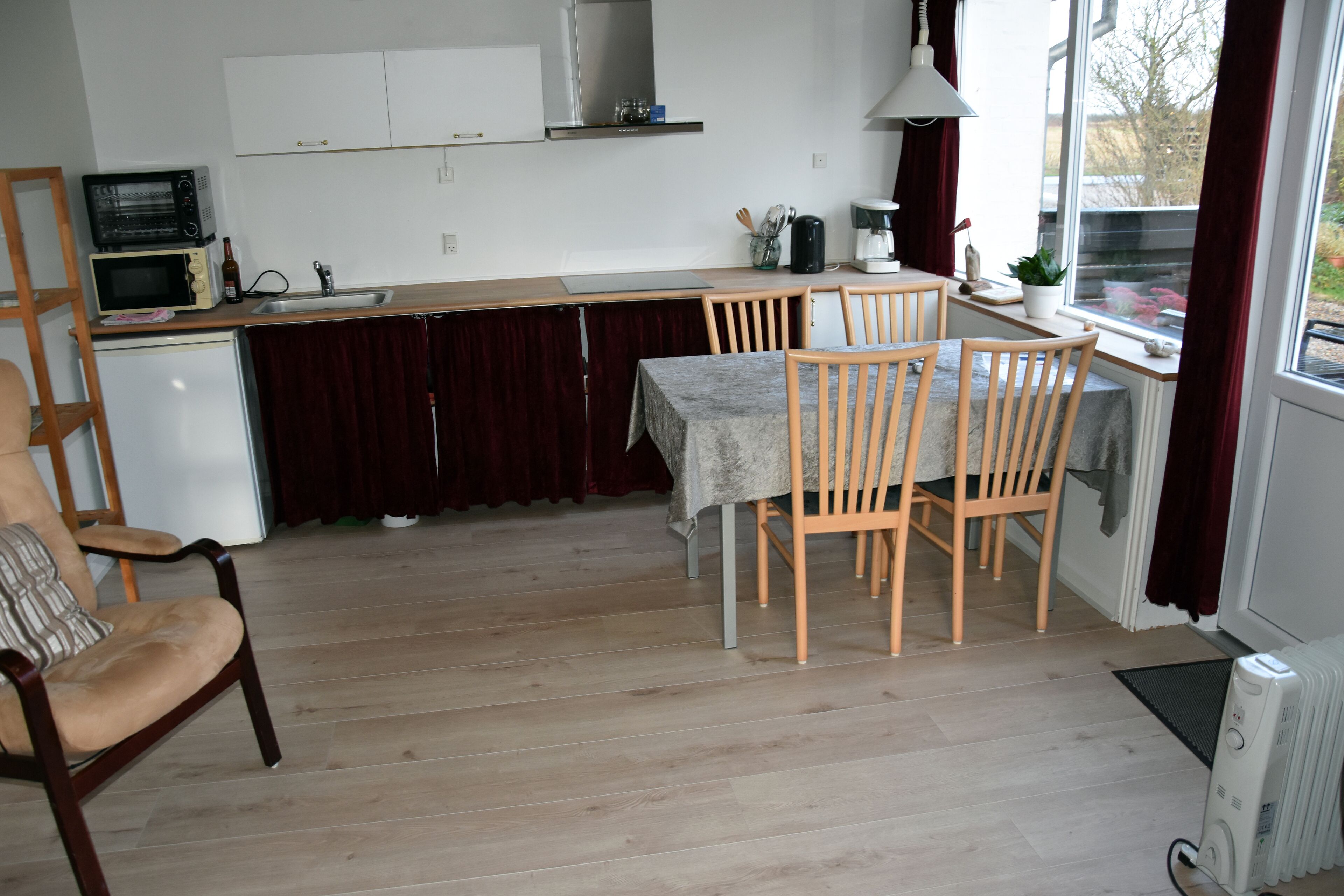 A compact kitchen with a dining area, wooden chairs, a table, and a view through a window.