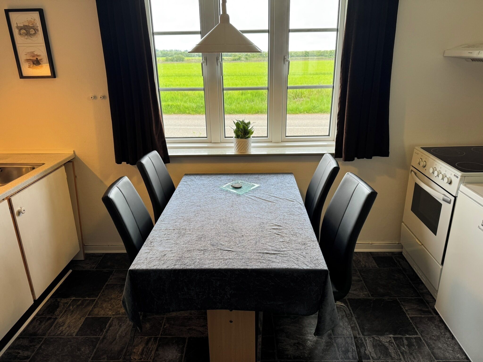 A compact kitchen with a dining table, chairs, a stove, and a window with a view of a green field.