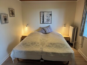 A bedroom with a bed, two bedside lamps, a radiator, and artwork on the walls. - Henne Strand Ferie (Norre Nebel)